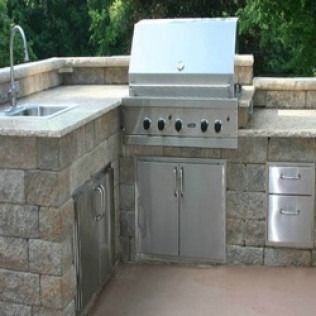 Outdoor kitchen with stone counters, stainless steel grill, sink, and cabinets.