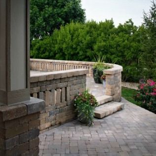 Stone patio with retaining walls, steps, and potted plants overlooking a green landscape.