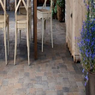 Brick-paved floor with dining chairs and rustic cabinet, purple flowers in a pot, warm colors.