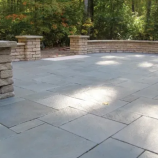 Blue stone patio with brick pillars and a curved retaining wall, surrounded by trees.