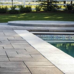 Poolside patio with gray pavers and a circular structure in the background, near a grassy lawn.