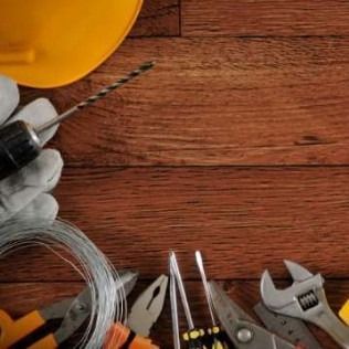 Work tools on wood background, including a drill, wire, gloves, and wrenches.