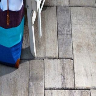 Patio pavers with a striped tote bag and white chair leg.