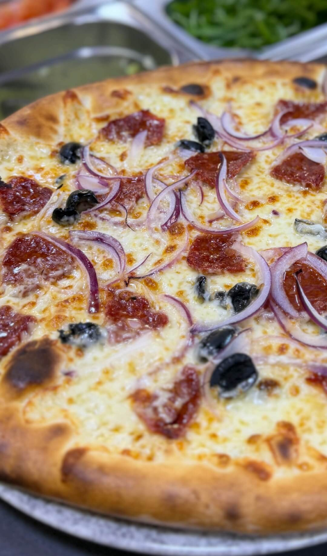 Una pizza condita con peperoni, olive nere e cipolle rosse tagliate a fettine sottili, su una base leggera e dorata.