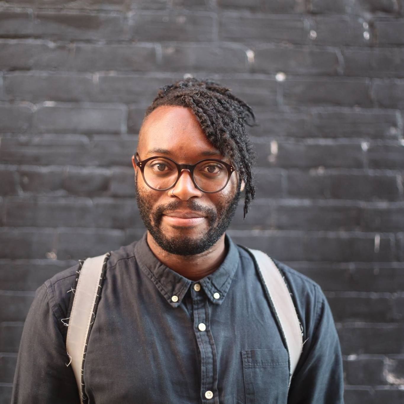 Aljumaine Gayle smiling directly at the camera in front of a grey brick wall.