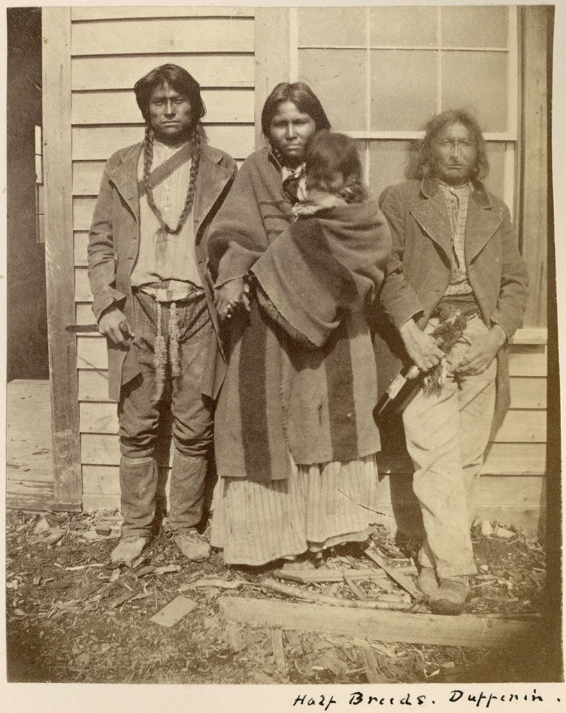 A sepia tone photo of 3 unidentified Metis people and a baby posed in front of a building at Dufferin