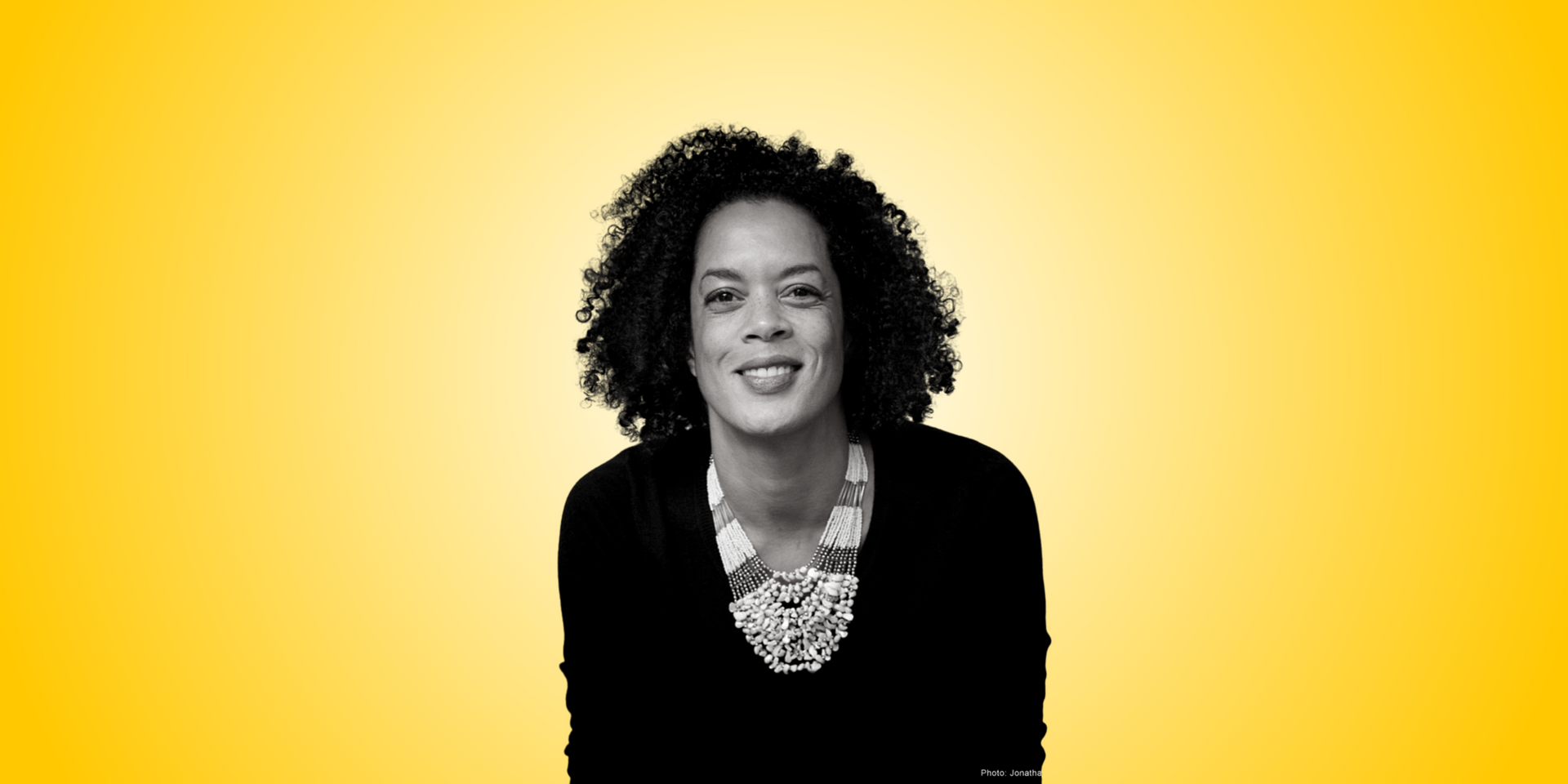 A woman with curly hair is smiling in a black and white photo.