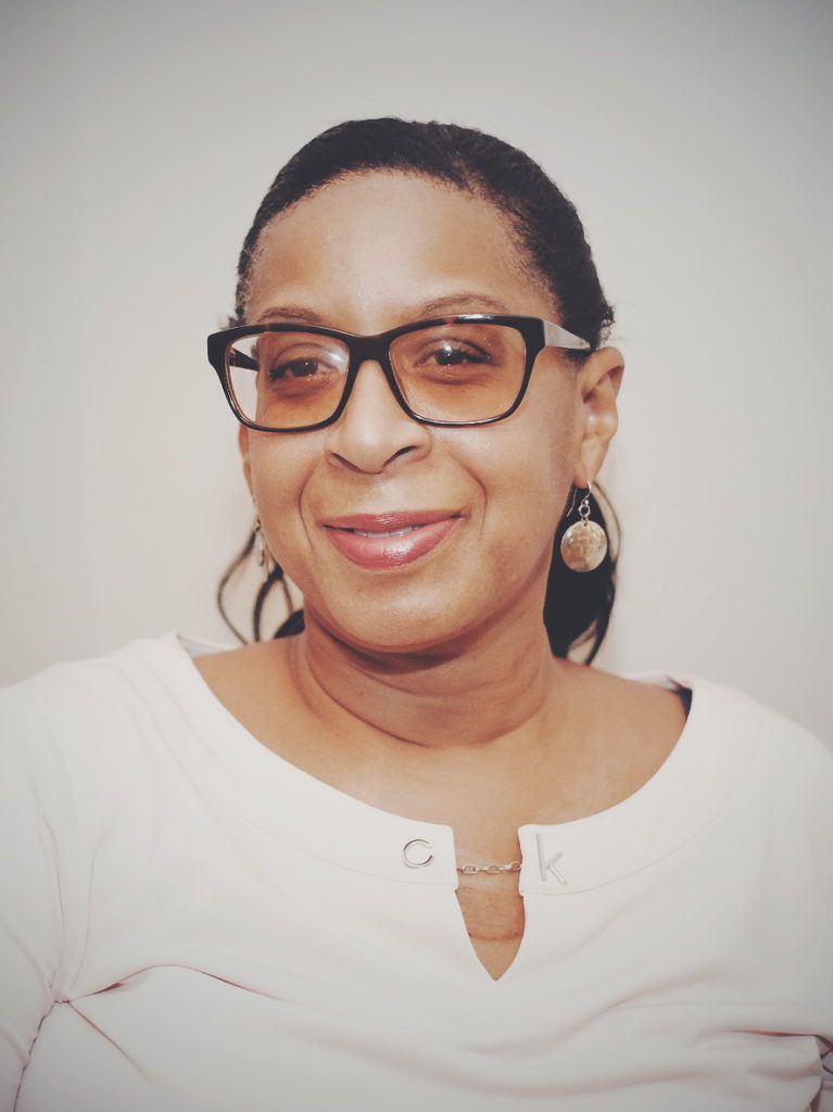 A woman wearing glasses and earrings is smiling for the camera