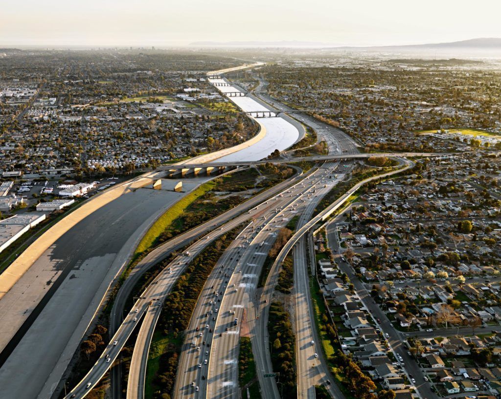 Header image for In the Wake of Progress showing a vast river and highway in the daytime.