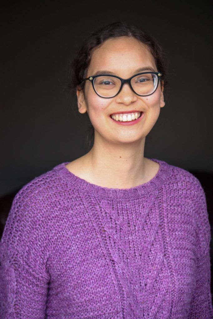 Built on Genocide research and writer, Mnawaate Gordon-Corbiere photo wearing glasses and a purple sweater with a bright smile