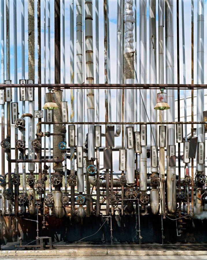 Edward Burtynsky's Oil Refinery is a wall of pipes lined up vertically with the blue sky showing between the pipes.