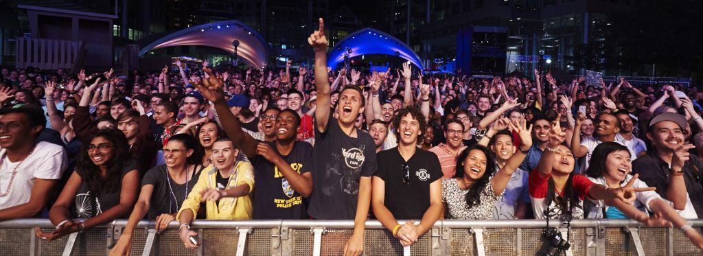 Photo of the audience at The Roots' performance during Luminato 2014. A large crowd of people are cheering and smiling at a live concert. 