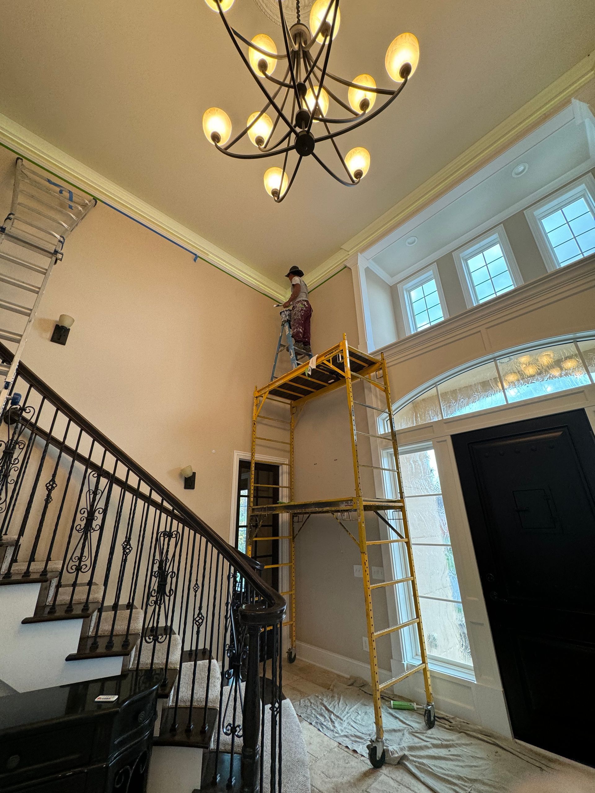 A man is standing on a scaffolding in a room with stairs and a chandelier.