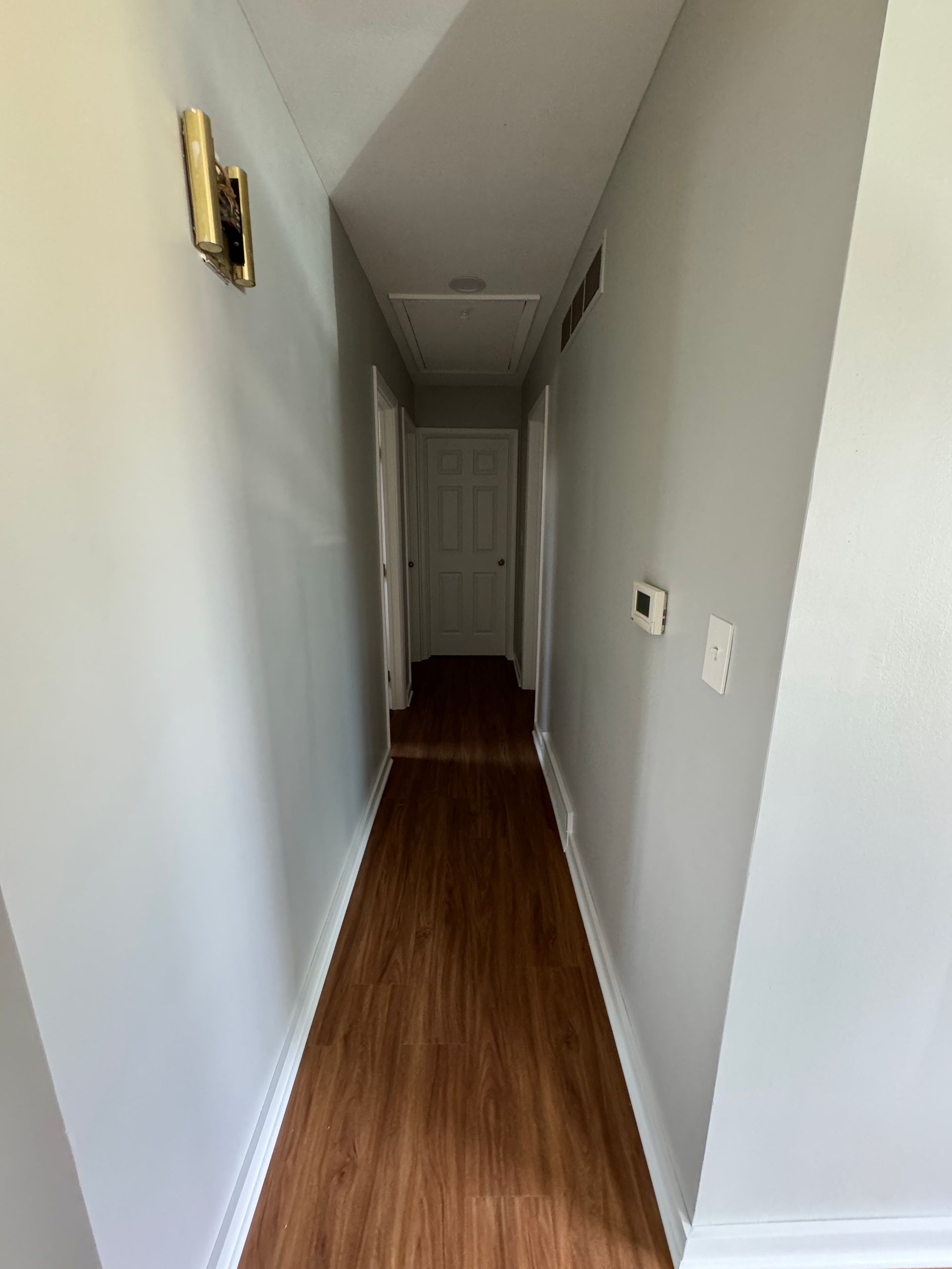 A long hallway with wooden floors and white walls in a house.