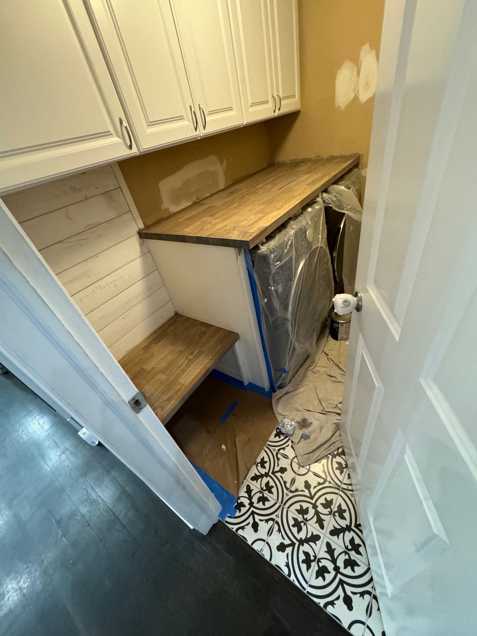 A laundry room with white cabinets and a wooden counter top.