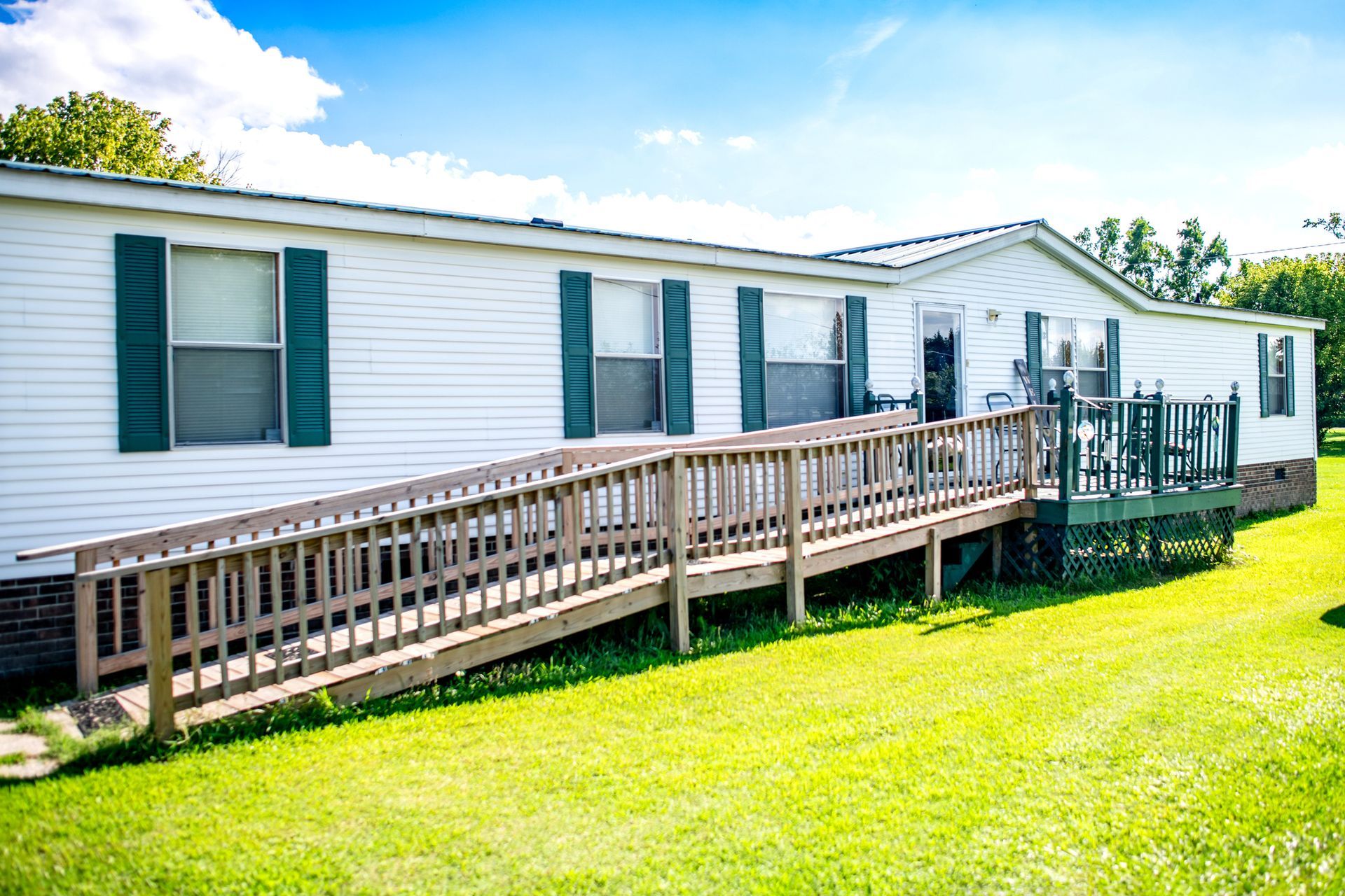 Accessible mobile home with ramp, porch, and trimmed lawn in sunny, peaceful neighborhood park. Accessible mobile home with ramp, porch, and trimmed lawn in sunny, peaceful neighborhood park.