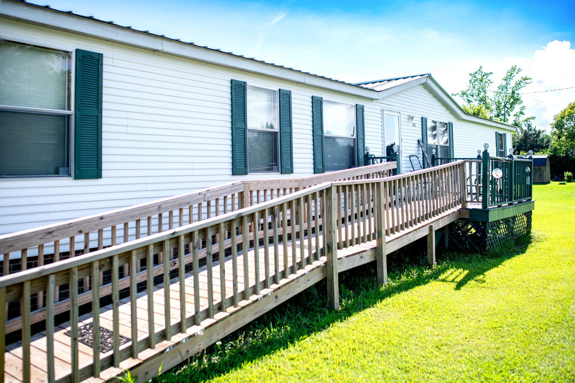 White mobile home with green shutters and wooden wheelchair ramp.