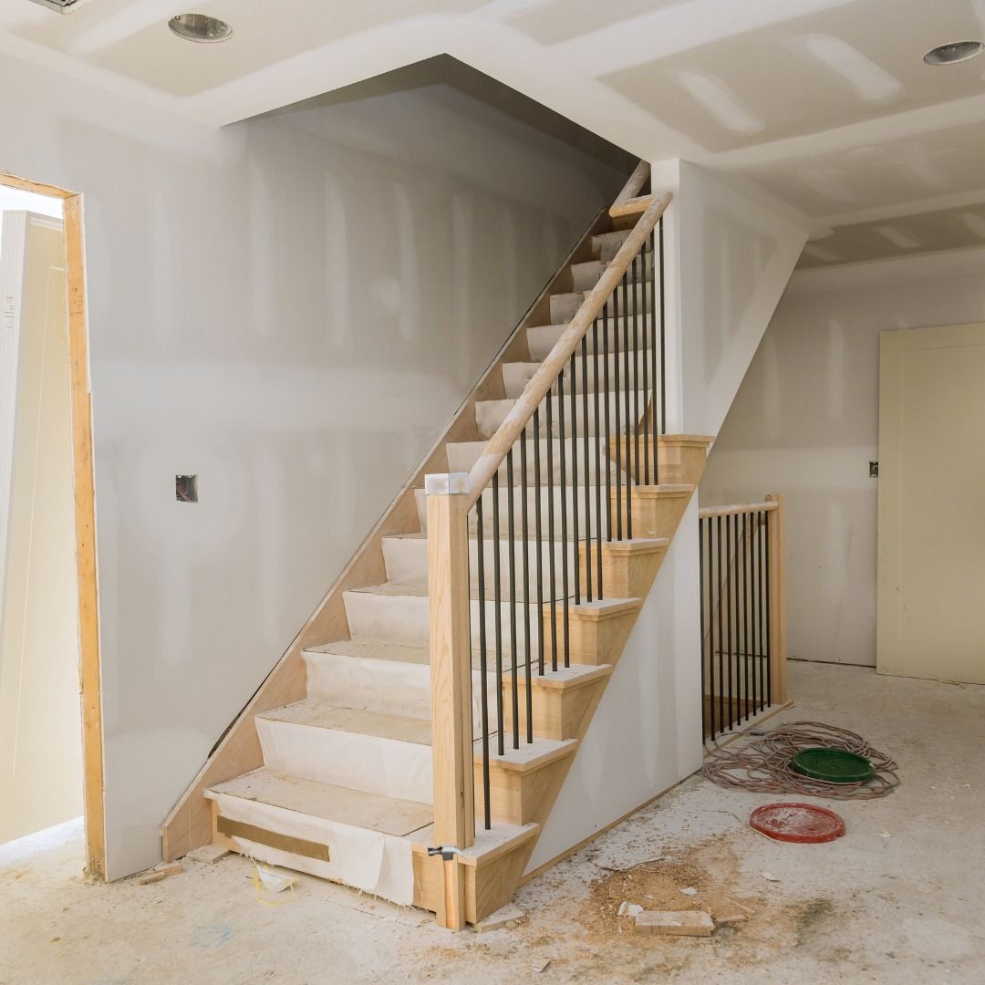 Staircase under construction, unfinished drywall, light wood steps, black metal railings, interior setting.