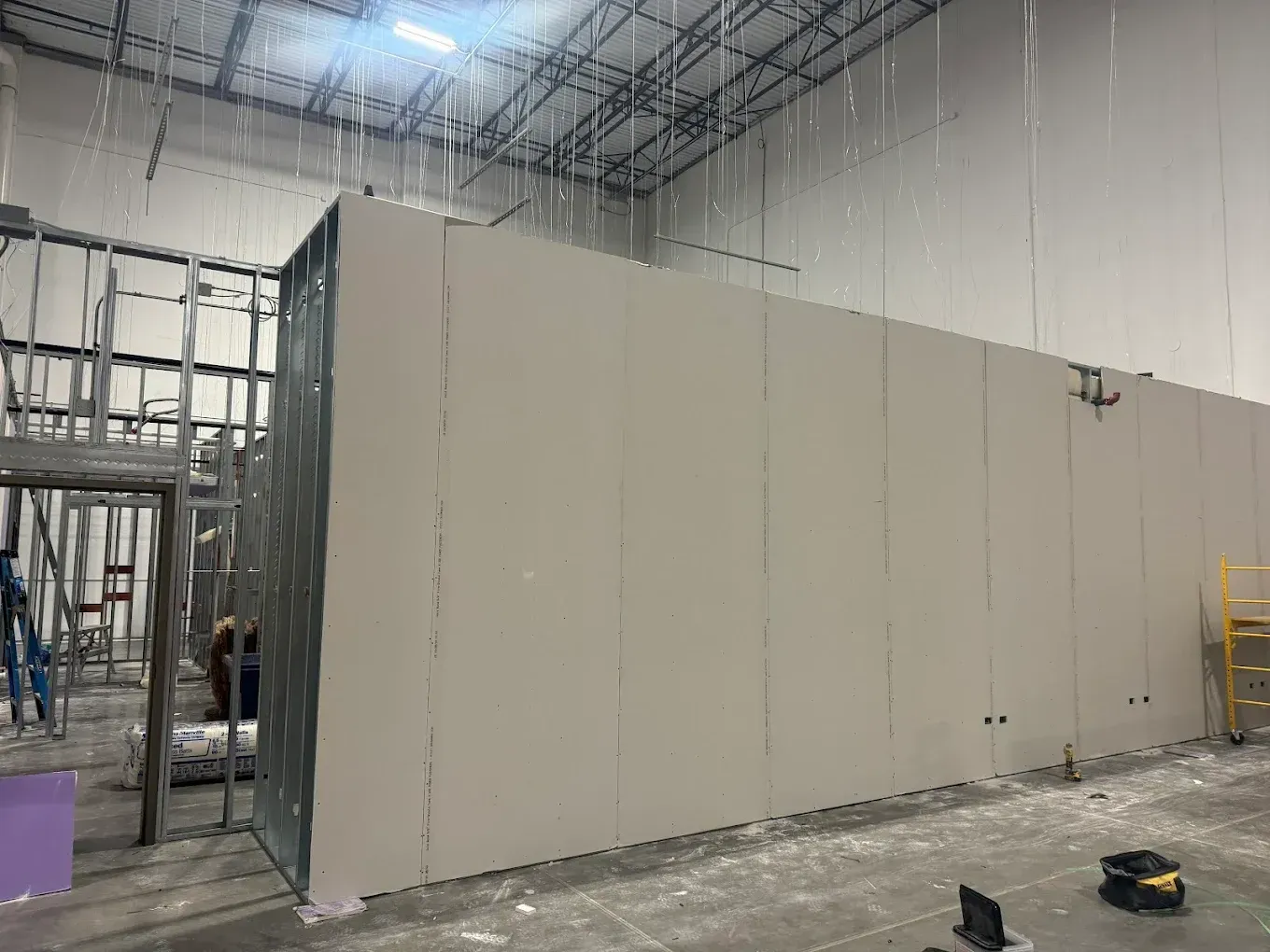 Construction of interior walls inside a warehouse. Steel framing, drywall, and unfinished surfaces are visible.