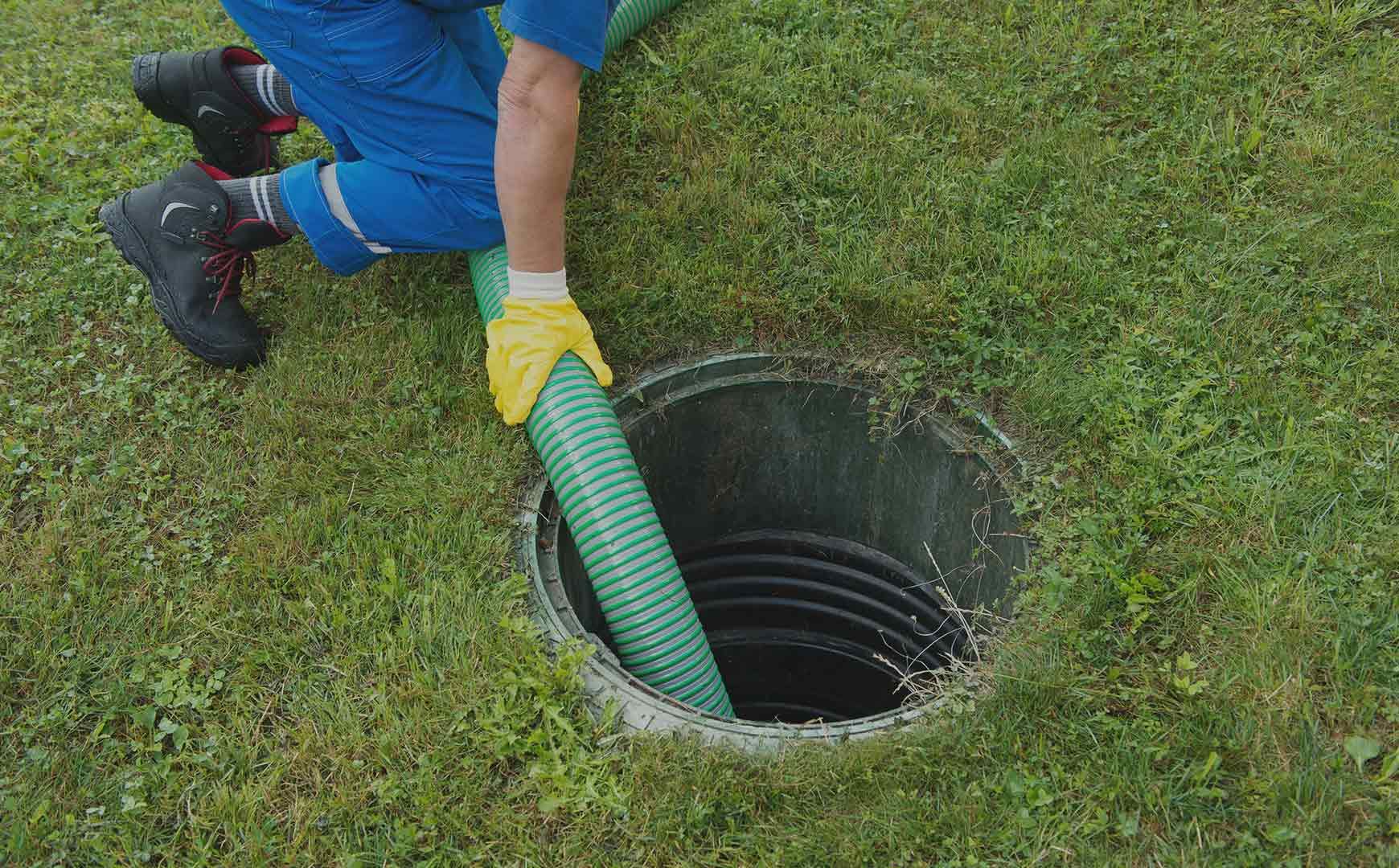 A man is pumping water into a septic tank with a green hose.