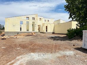 House under construction with light blue foam walls and wooden roof frame on a hillside.
