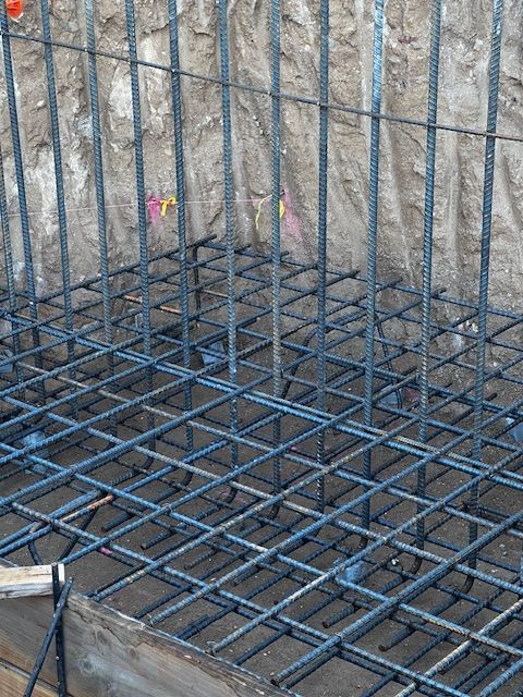 Reinforced steel grid (rebar) in a construction site, set in a rectangular formation against a dirt wall.