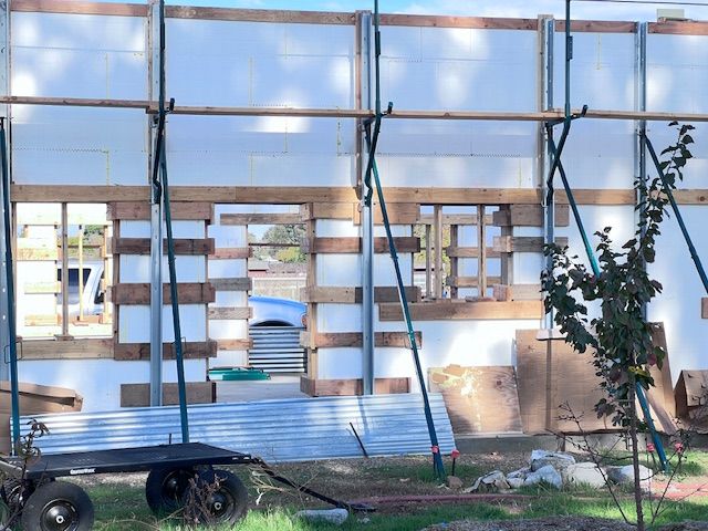 Construction site with wood frame and foam insulation; a cart and corrugated metal are in the foreground.
