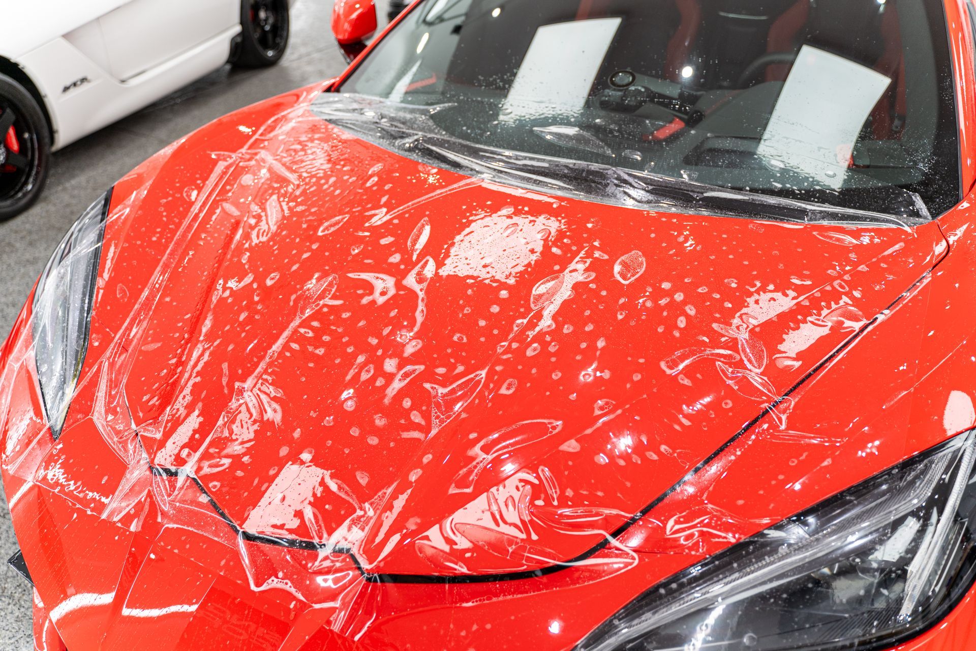 The hood of a red sports car is wrapped in plastic.