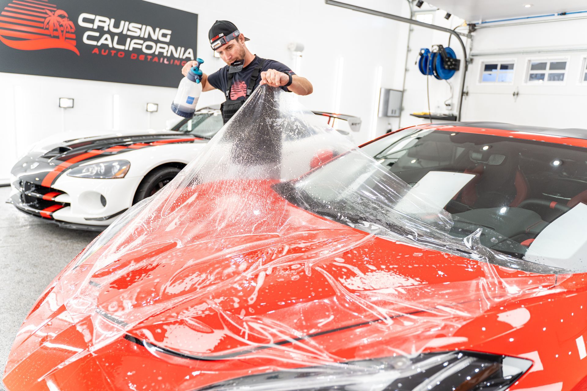 A man is wrapping a red sports car with plastic.