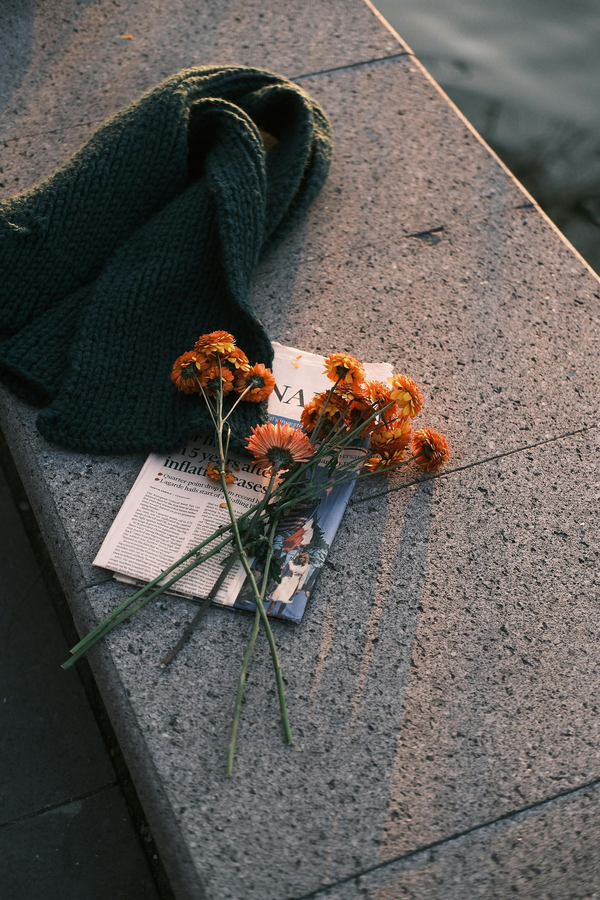 A scarf and flowers are sitting on a bench next to a book.