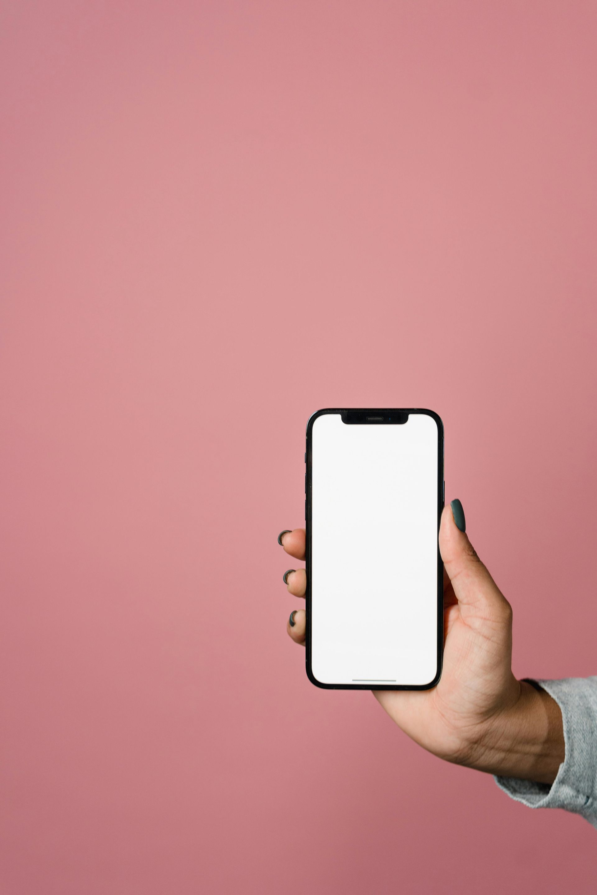 A woman is holding a cell phone with a blank screen against a pink background.