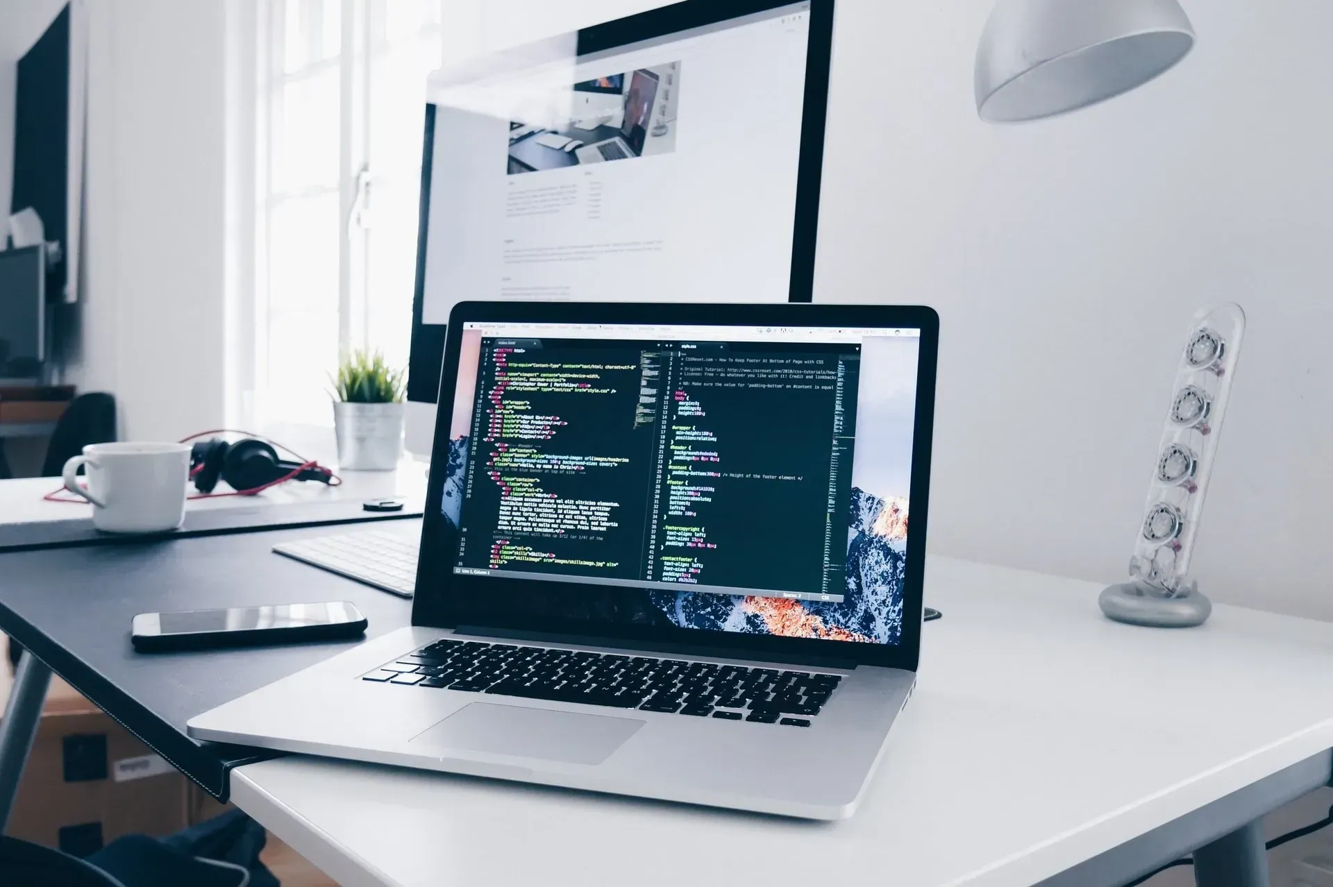A laptop computer is sitting on a desk next to a monitor.