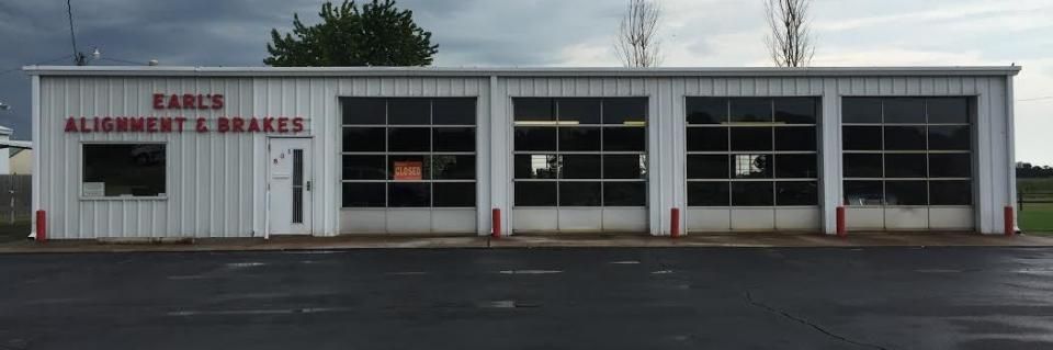 White building with Earl's Alignment & Brakes sign, glass garage doors, red accents, and a dark overcast sky.