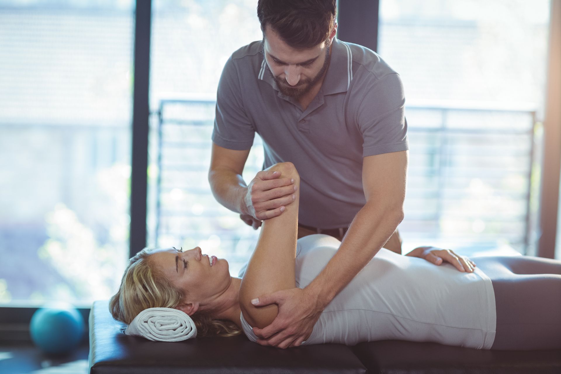 A therapist is assisting a woman with targeted shoulder rehabilitation exercises.