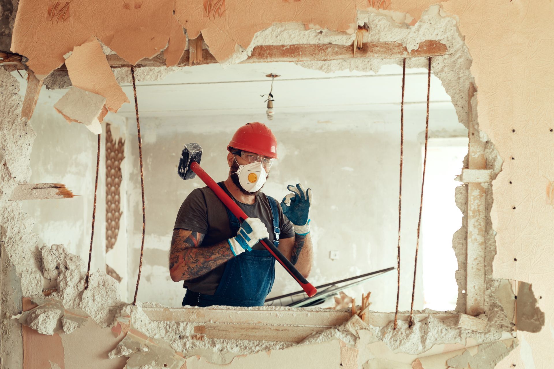 Worker with a hammer standing in front of a wall with a hole in it