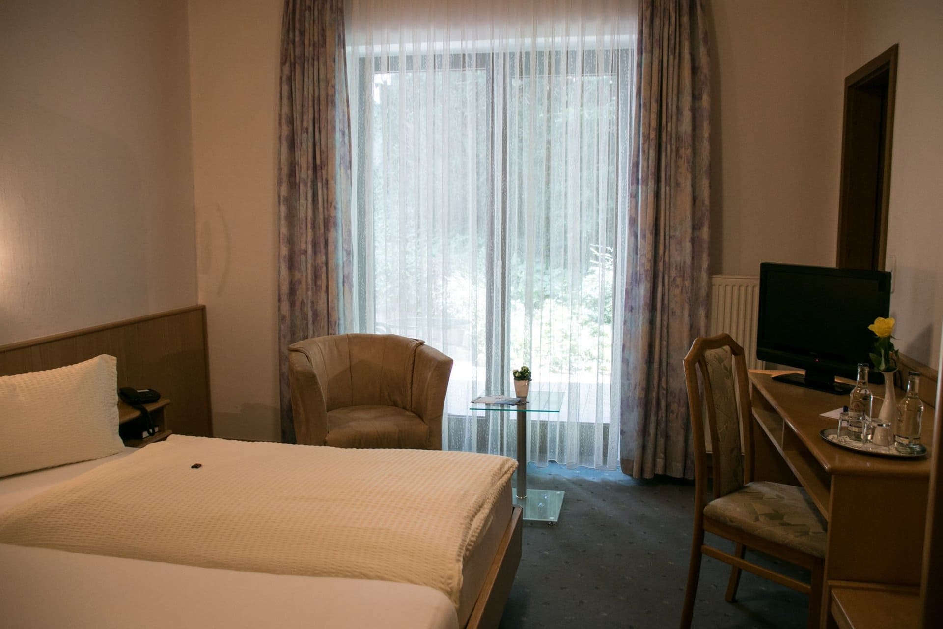 Ein Hotelzimmer mit zwei Betten, einem Stuhl, einem Schreibtisch und einem Fernseher.