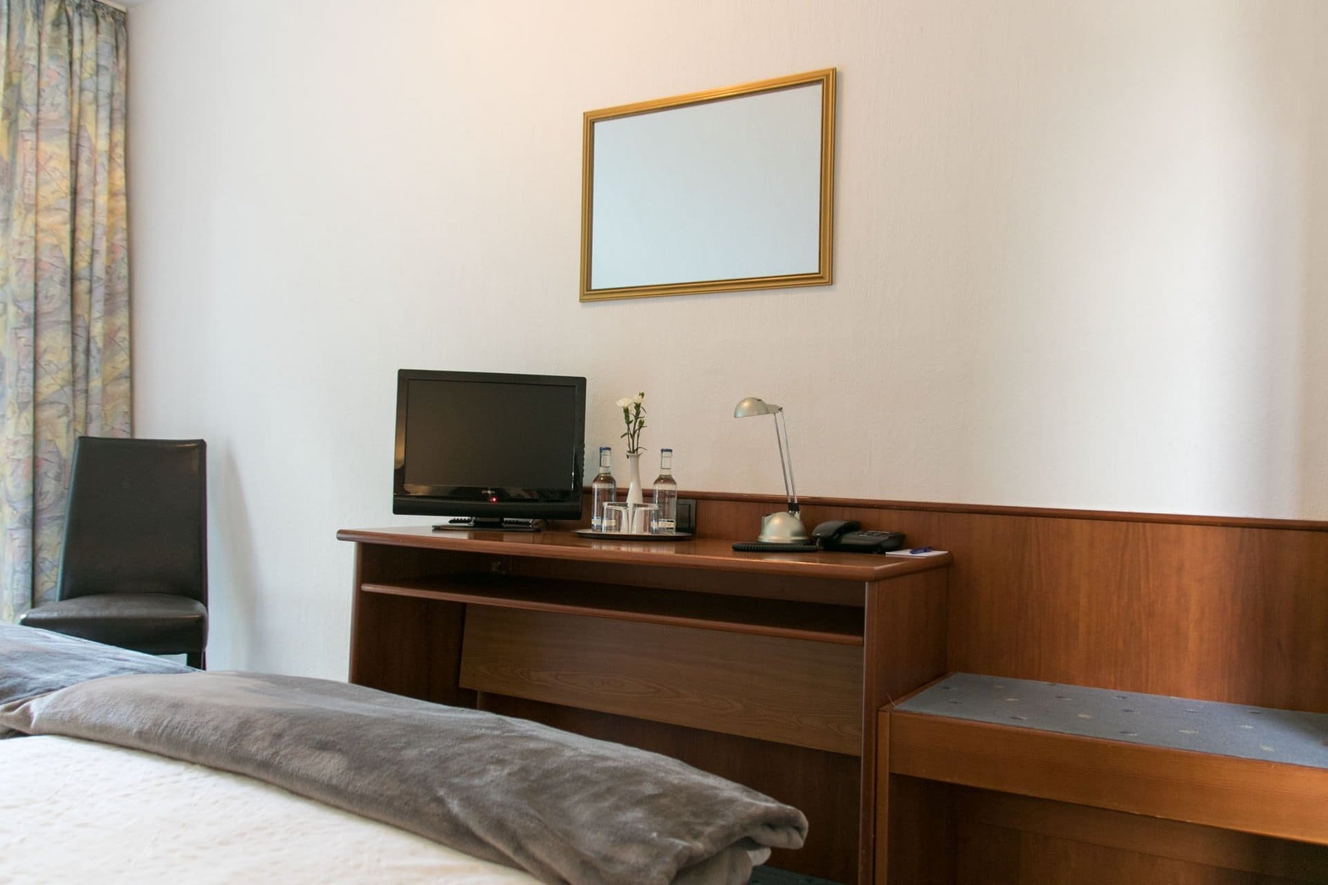 Ein Hotelzimmer mit Bett, Schreibtisch, Fernseher und Spiegel.