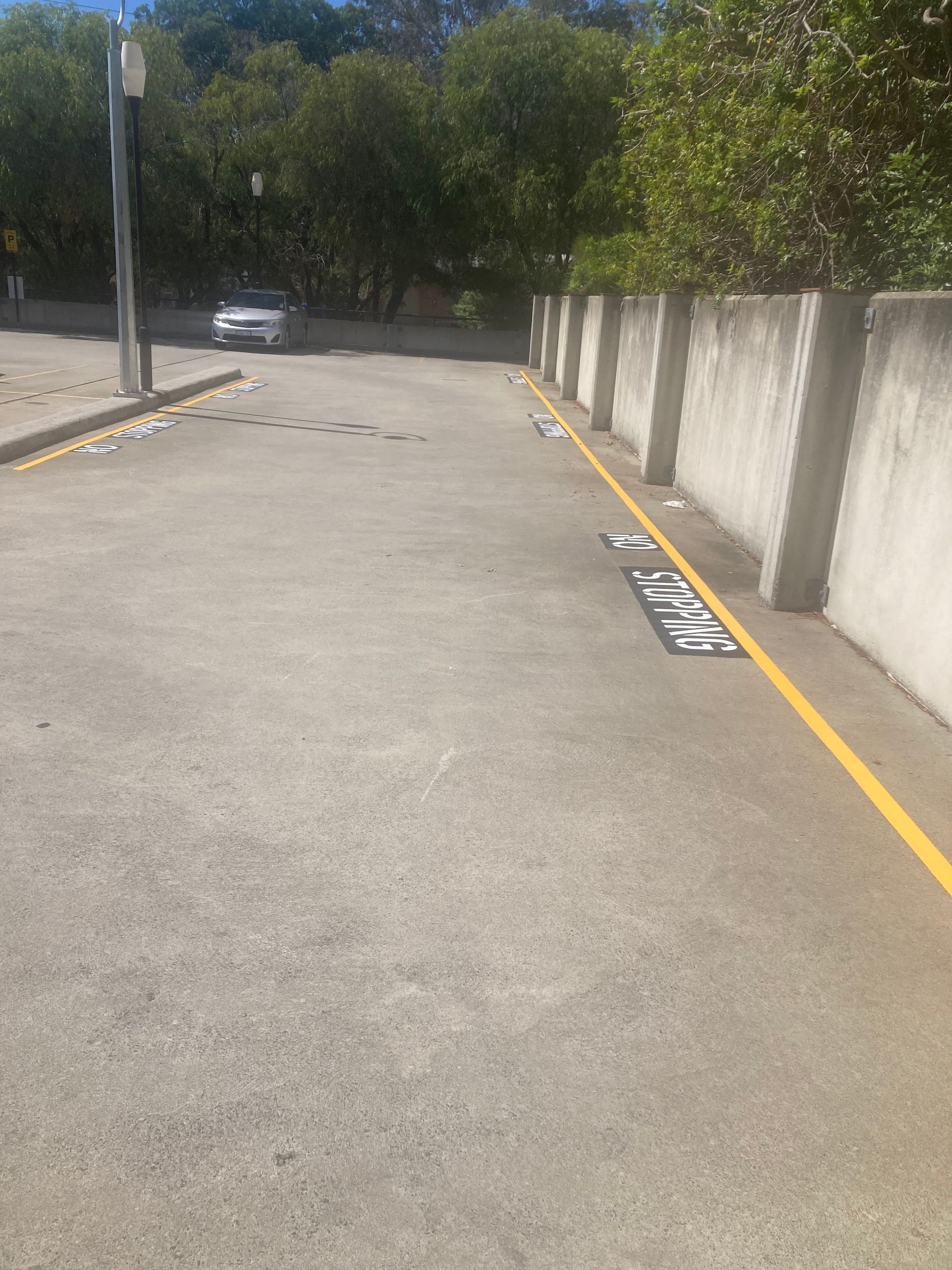 Concrete driveway with yellow lines, wall to the right, and a car in the distance.