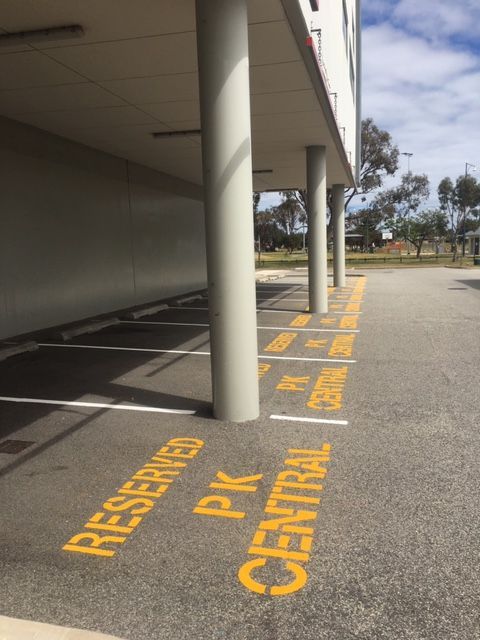 Parking area with reserved spaces marked with yellow paint; located beneath a building with support columns.