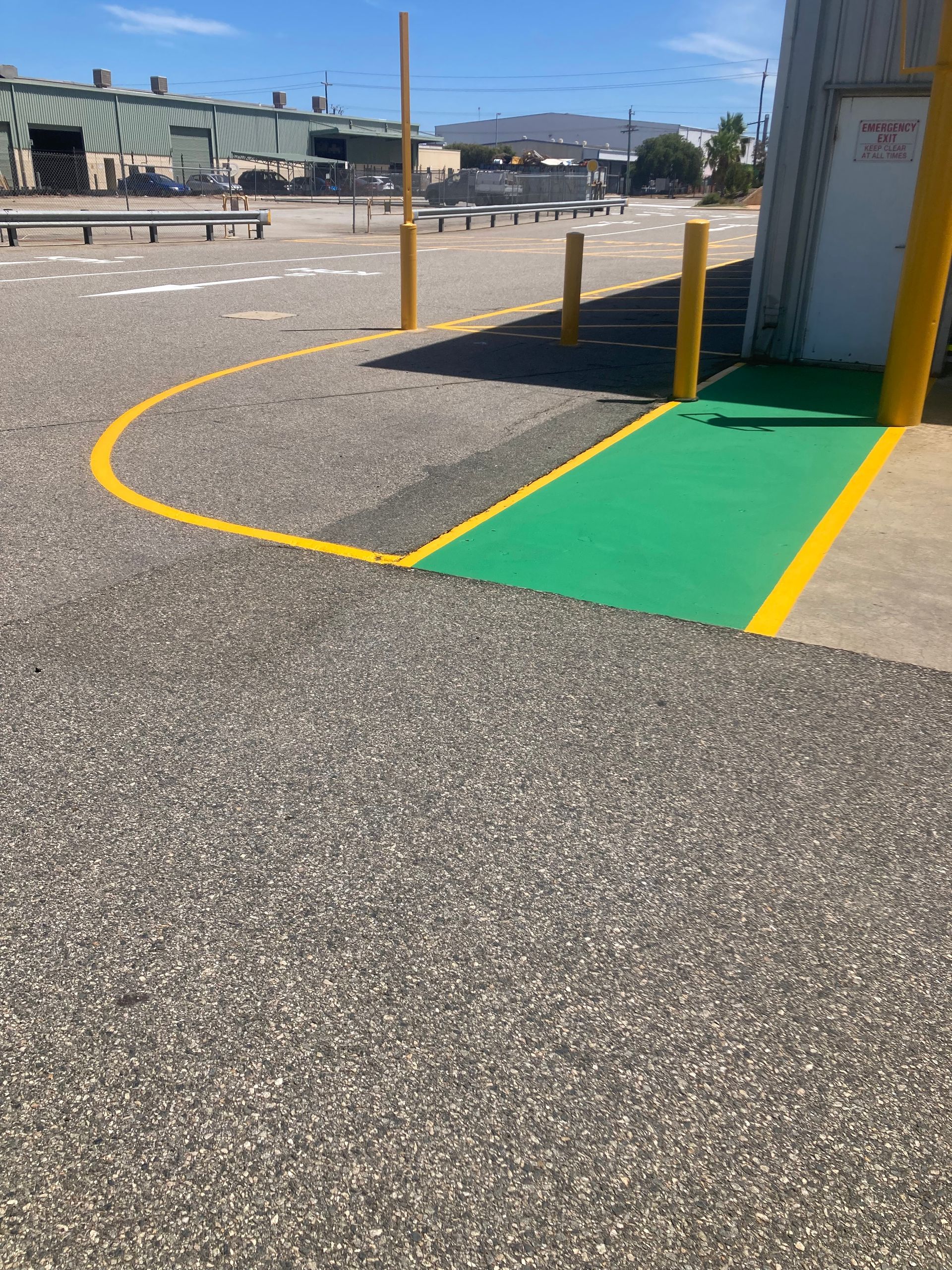 A green painted loading dock area with yellow lines and bollards. Outdoors, industrial setting.