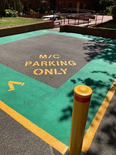 Motorcycle parking spot marked with green and yellow paint, featuring a yellow bollard.