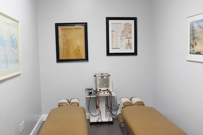 Two massage tables face a medical device; walls have framed diagrams.