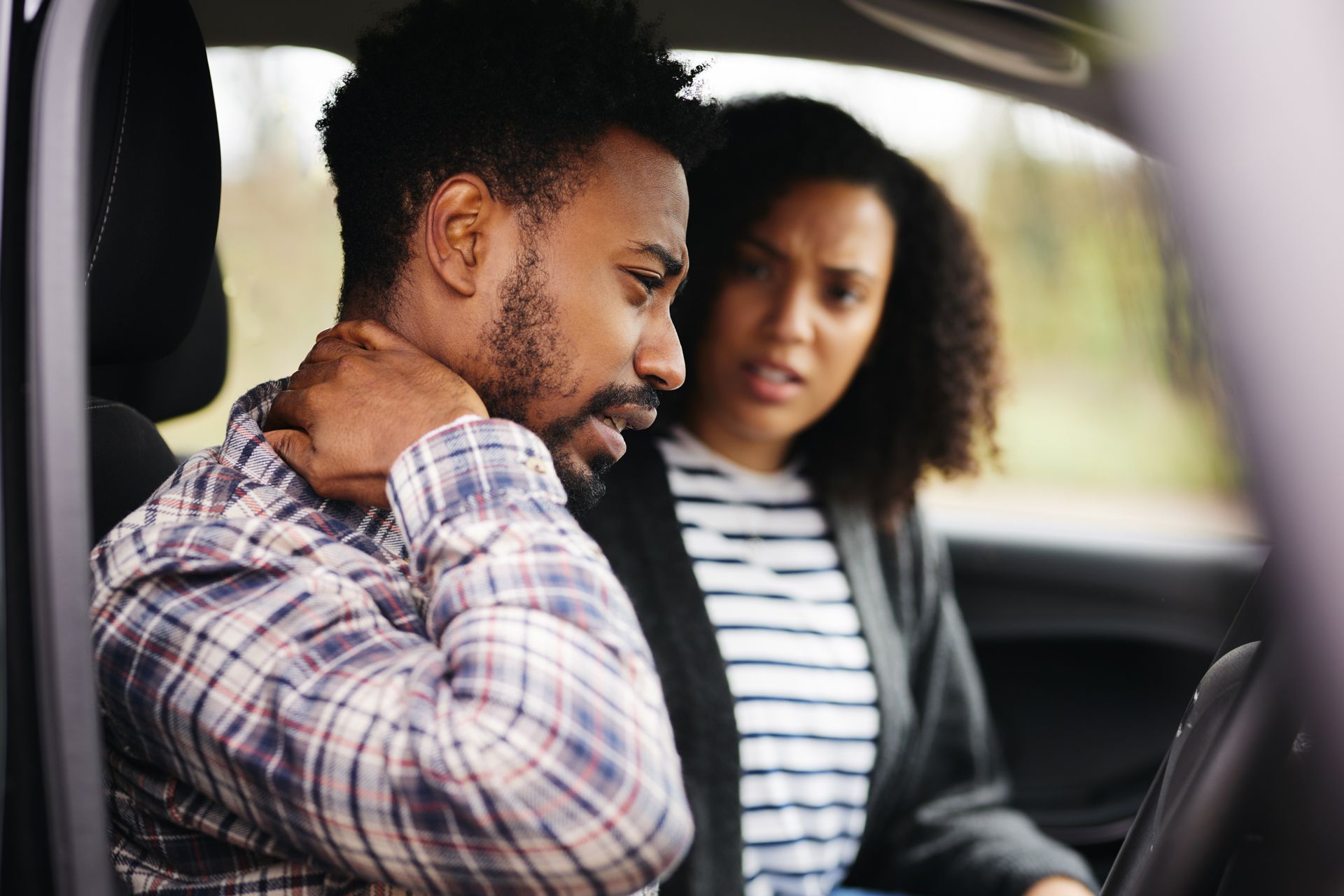 Man in car holding his neck, woman looking concerned.