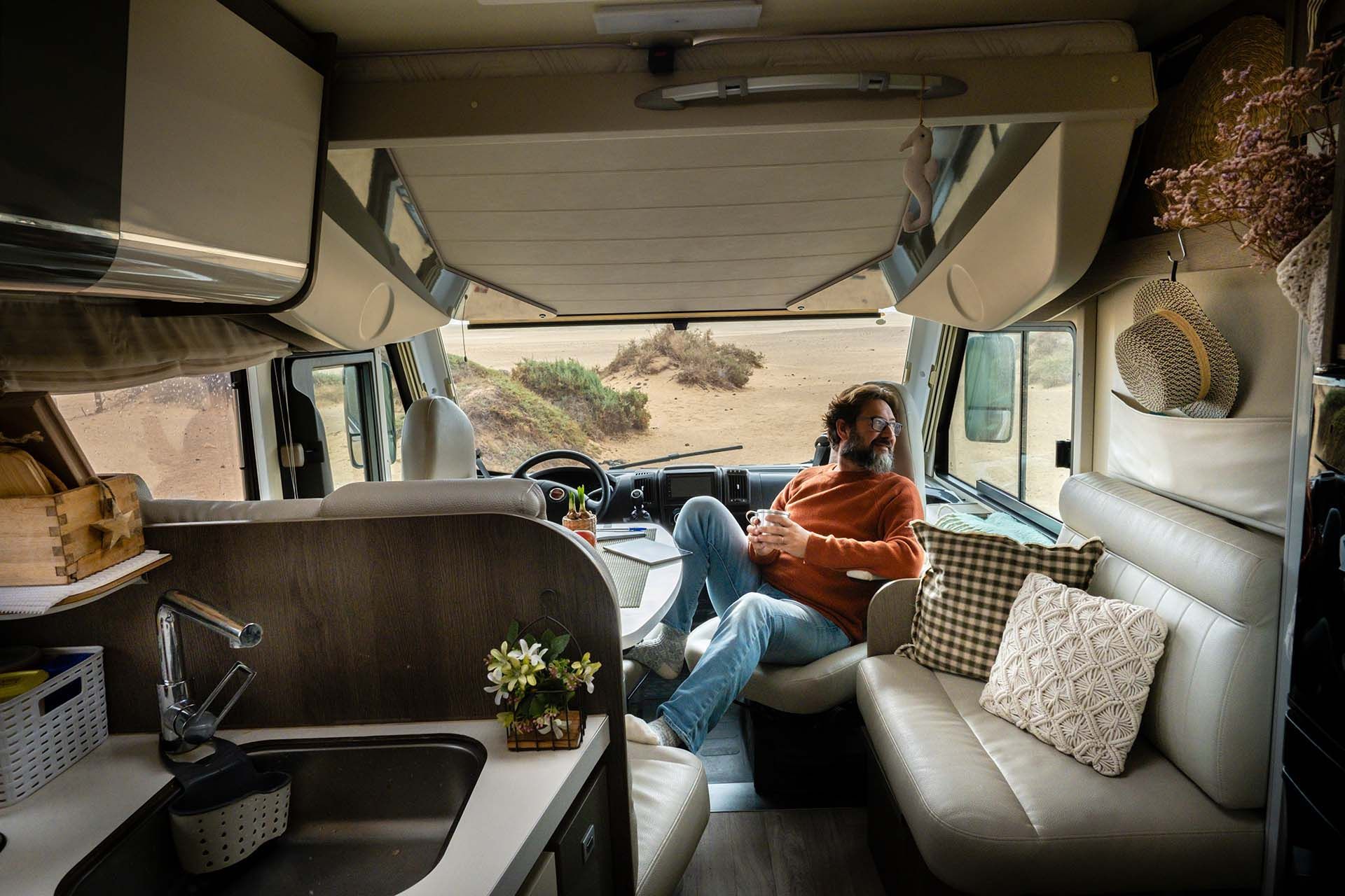 Interior of a camper van with seating, kitchenette, and wide front view overlooking a landscape.