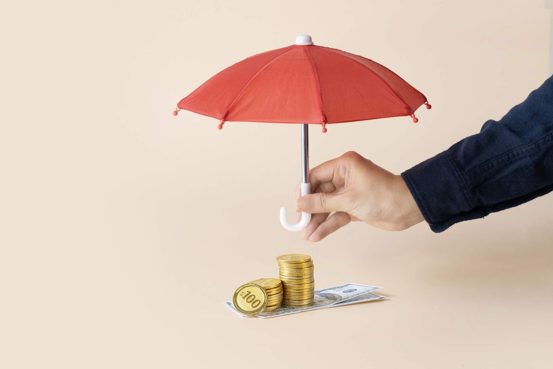 Hand holding a red umbrella over a stack of coins and notes. Hand holding a red umbrella over a stack of coins and notes.
