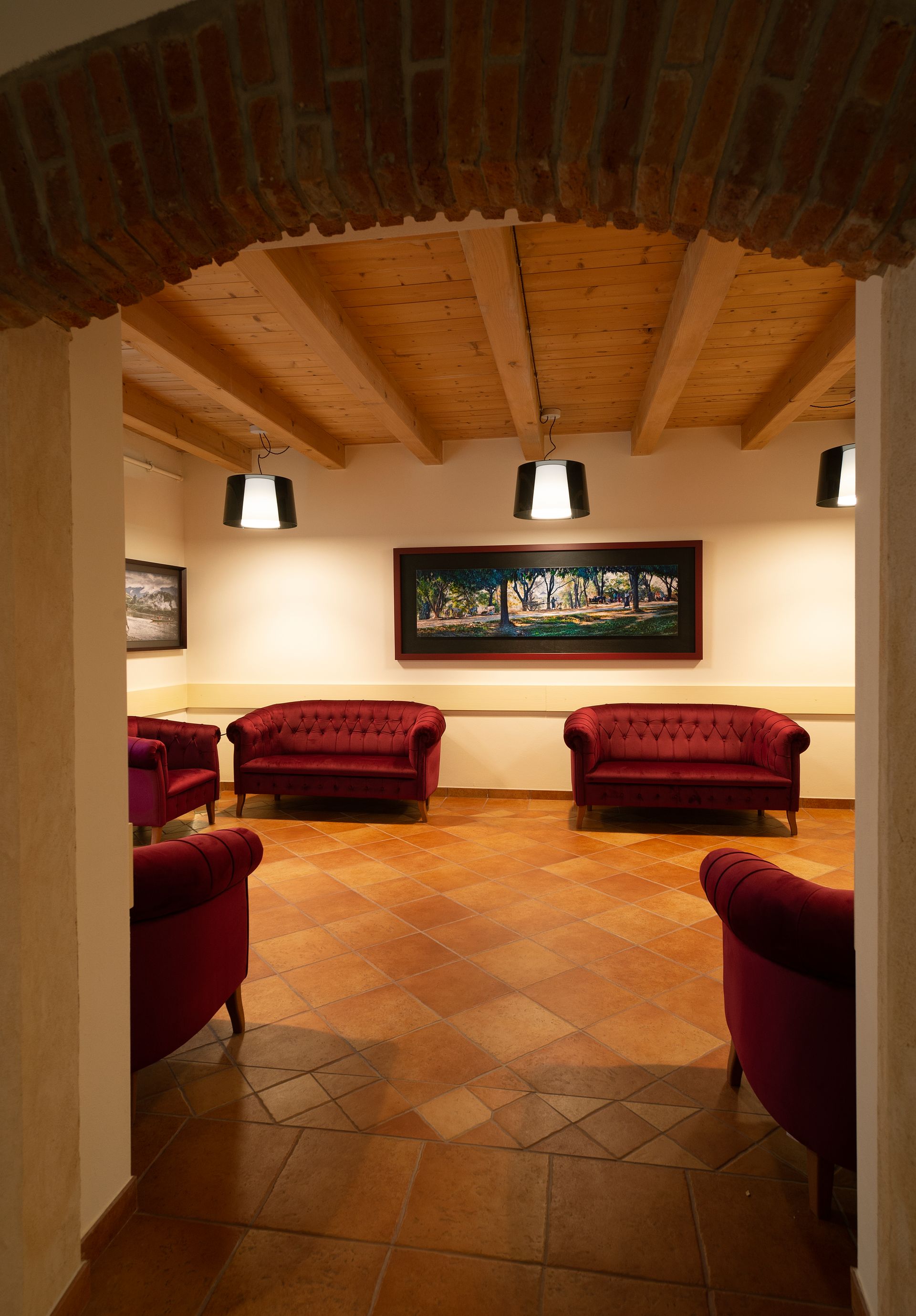 Accogliente salotto con poltrone rosse, soffitto a volta in mattoni e quadri incorniciati alle pareti, su un pavimento in piastrelle dai toni caldi.