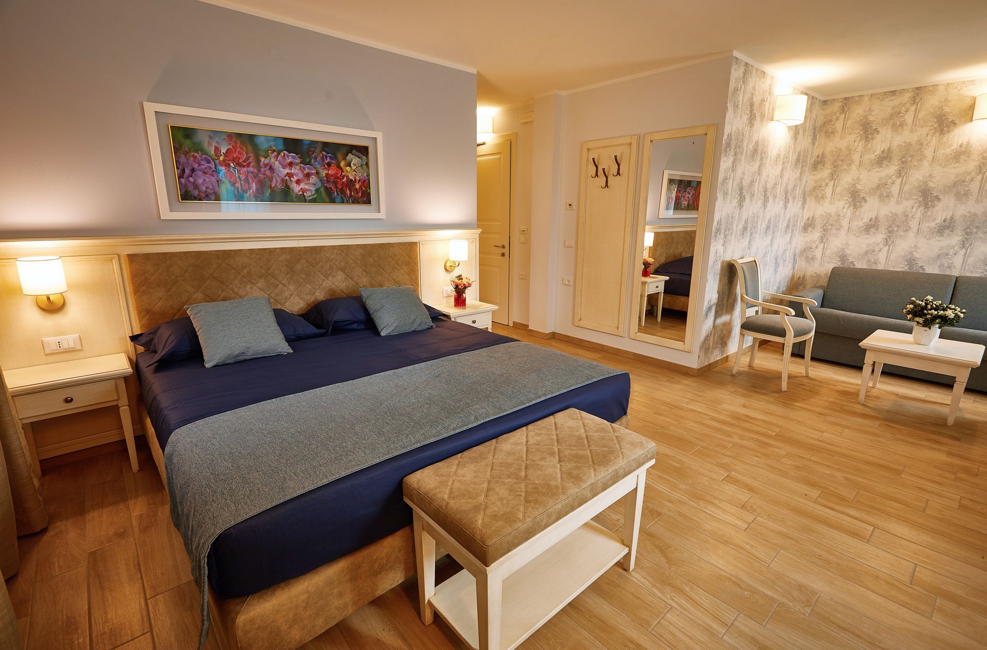 Camera da letto moderna con un grande letto, biancheria da letto blu, pavimento in legno e illuminazione calda.