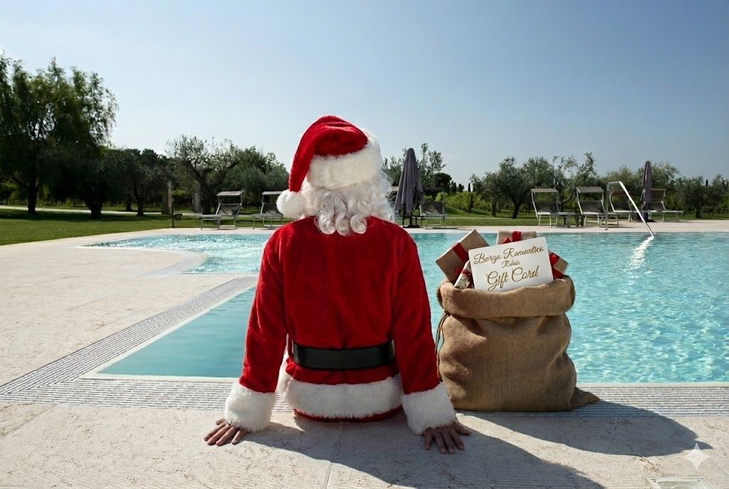 Una persona vestita da Babbo Natale in rosso siede a bordo piscina accanto a un sacco di regali.