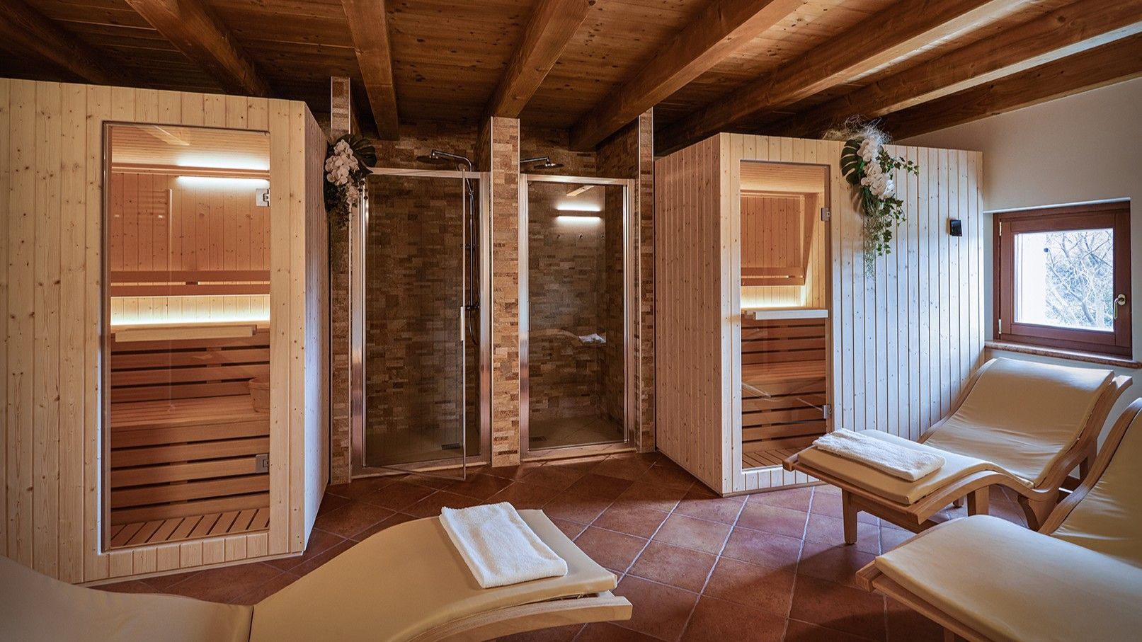 Sauna con pannelli in legno, porte in vetro, panche in legno e poltrona relax vicino a una finestra.