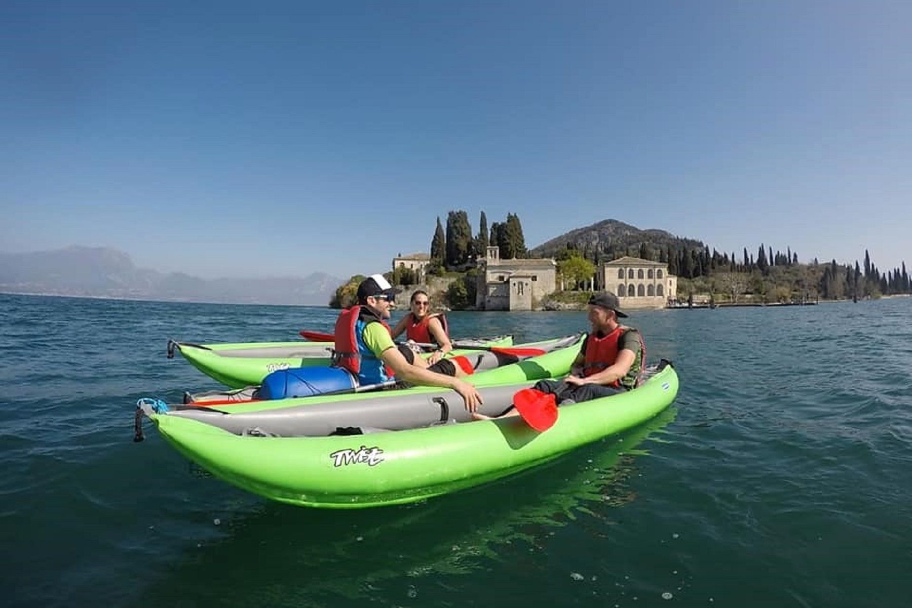 Persone in kayak su un lago blu vicino a un castello di pietra e alberi sulla riva.